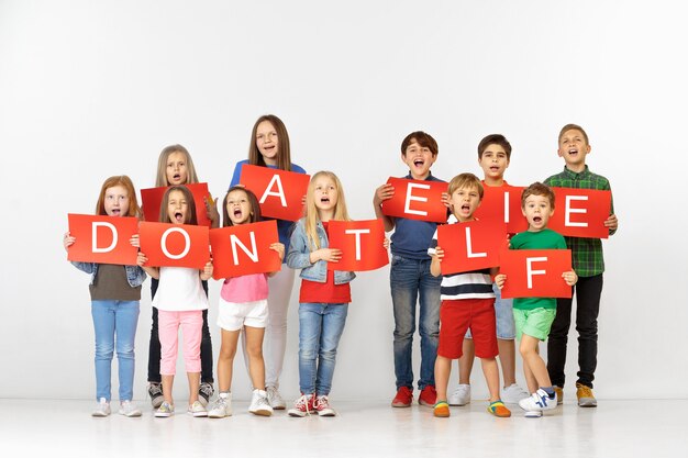 Donner la vie. Groupe d'enfants qui crient avec des bannières rouges faisant un mot isolé sur fond de studio. Concept d'éducation et de publicité. Concepts de protestation et de droits de l'enfant.