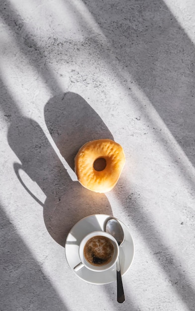 Photo un donut appétissant à côté d'une tasse de café baigné dans la lumière naturelle vue de haut