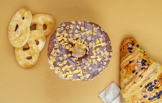 Donut au chocolat frais, croissant et biscuit isolés sur fond délicat de café ou marron. Desserts délicieux. Concept d'aliments sucrés pour votre conception et impression. Vue de dessus, mise à plat. Espace de copie.