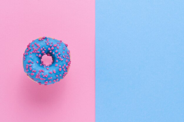 Donut bleu saupoudré. Beignet saupoudré glacé sur fond bleu rose. Vue de dessus, copiez l'espace.