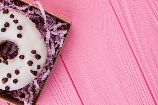 Donut dans la boîte, copiez l'espace. Beignet glacé sur fond de bois rose. Espace pour le texte.