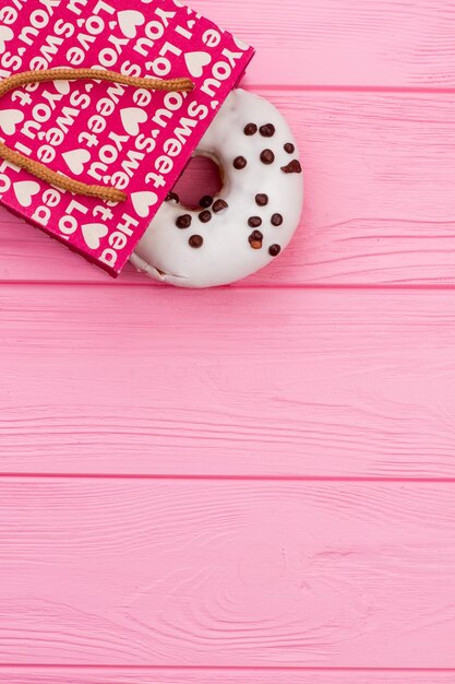 Donut dans un sac à provisions sur fond en bois. Cadeau doux pour la fête de vacances, vue de dessus. Espace pour le texte.