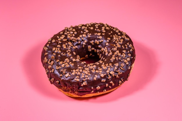 Donut avec glaçage au chocolat sur le dessus isolé sur fond rose