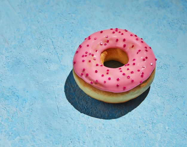 Donut avec glaçage rose et arrose sur fond bleu.