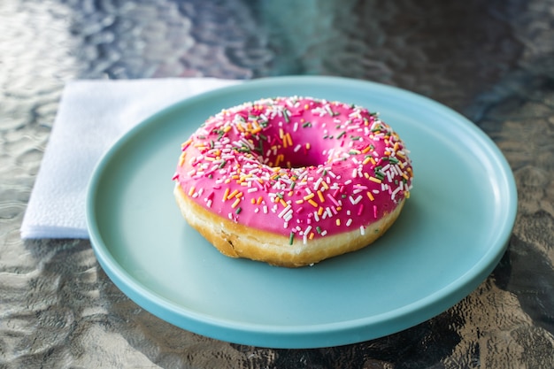 Donut glacé rose frais sur une plaque bleu turquoise. Notion de petit-déjeuner