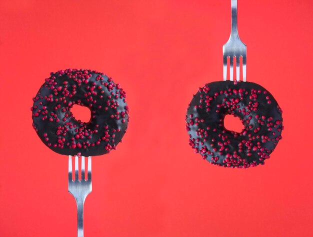 Donut avec glaçure noire empalé sur une fourchette d'argent sur le gros plan de fond rouge