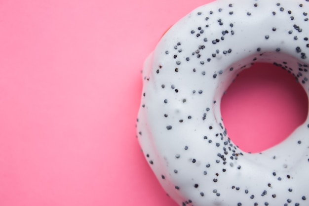 Donut rond fait maison avec glaçage blanc et graines de pavot saupoudré sur le rose tendre tendance situé sur le côté droit.