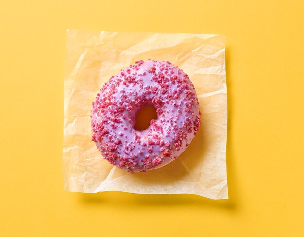 Donut rose sur fond de papier jaune, vue de dessus