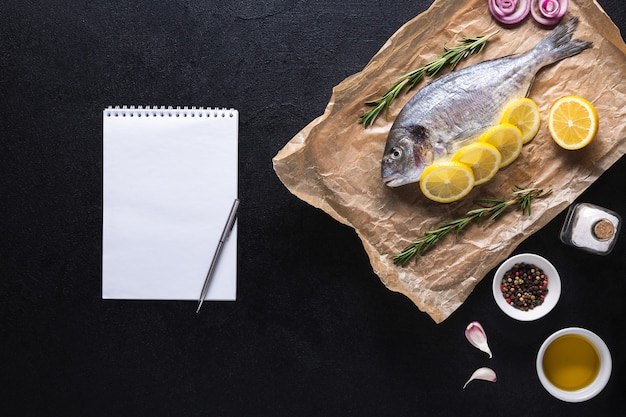 Dorado cru sur du papier de cuisson avec un cahier pour la recette Vue de dessus sur fond noir