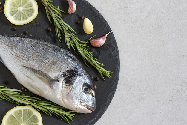 Un dorado ou une dorade biologique de mer crue fraîche avec des épices et du citron sur un fond gris Copiez l'espace