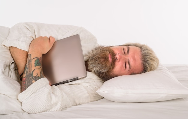 Photo dormir homme barbu dormir avec un ordinateur portable travailler à domicile homme barbu au lit le matin et réveiller l'homme
