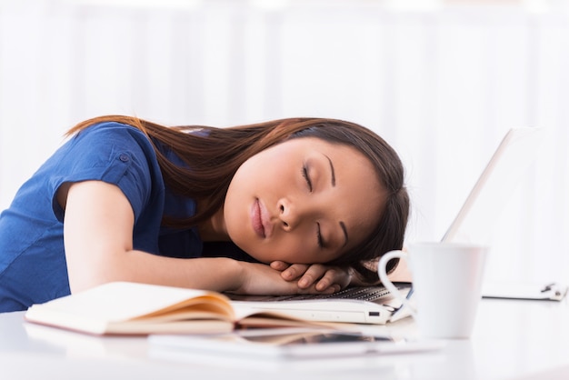 Dormir sur le lieu de travail. Belle jeune femme asiatique dormant sur son lieu de travail