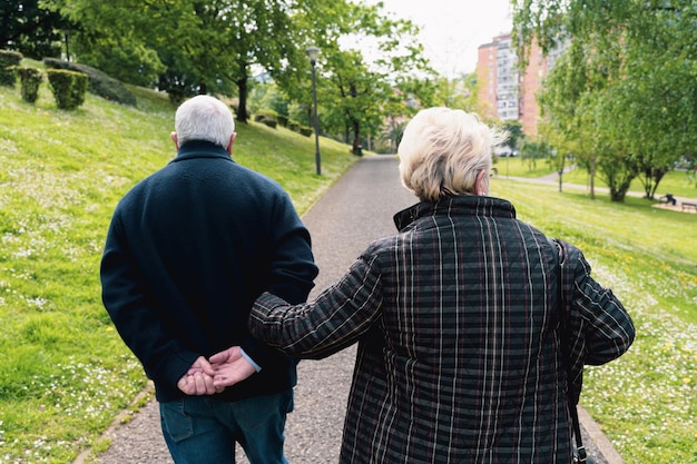 Dos du couple senior marchant dans le parc Femme âgée tenant le bras de son mari à l'extérieur