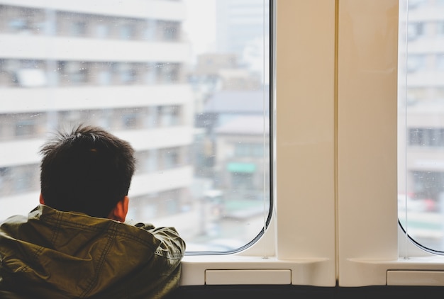 Photo dos du petit garçon voyageant en train et en regardant par la fenêtre en verre