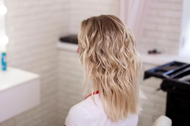 Dos féminin avec des cheveux blonds bouclés ombre dans un salon de coiffure