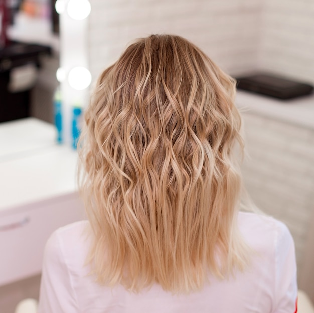 Dos féminin avec des cheveux blonds bouclés ombre dans un salon de coiffure