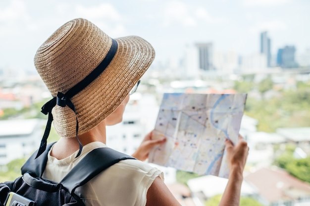 Dos de fille voyageur cherchant la bonne direction sur la carte, voyageant le long de l'Asie