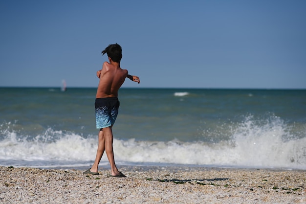 Dos de garçon jeter des cailloux dans la mer en plage Porto Sant Elpidio Italie