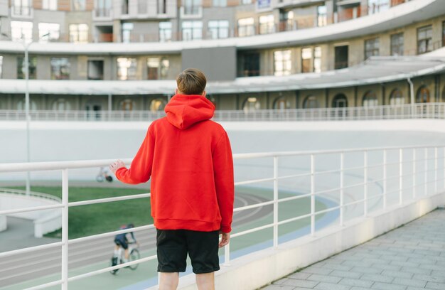 Le dos d'un jeune homme vêtu d'un sweat à capuche rouge se tient dans la rue et regarde le vélodrome