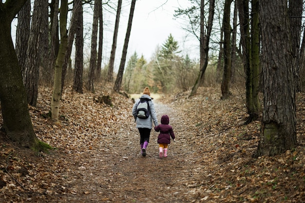 Dos de maman avec sac à dos et fille marchant le long de la forêt après la pluie ensemble