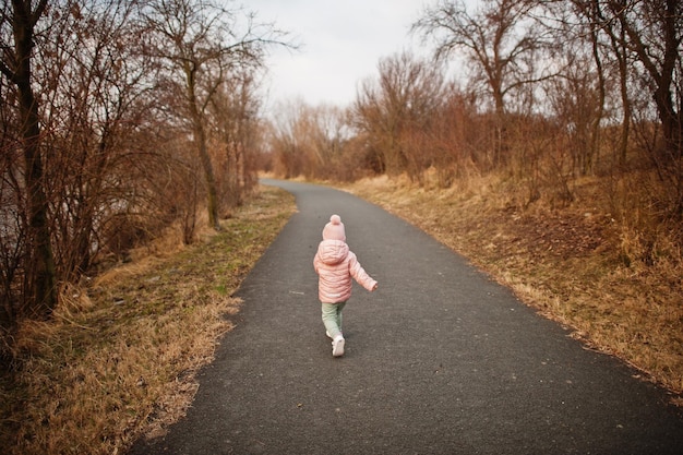 Dos d'une petite fille en cours d'exécution en veste rose sur le chemin