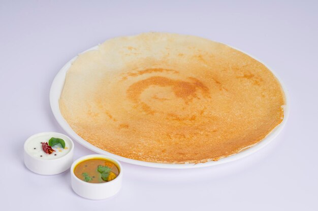 Dosa Ghee rôti Dosacélèbre petit-déjeuner du sud de l'Inde qui est fabriqué dans une poêle en fonte de manière traditionnelle et disposé sur une assiette blanche avec un plat d'accompagnement sur un fond blanc isolé