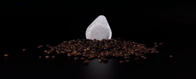 Photo dosette de papier à café pour l'espresso posée sur des grains de café frais sur un fond sombre