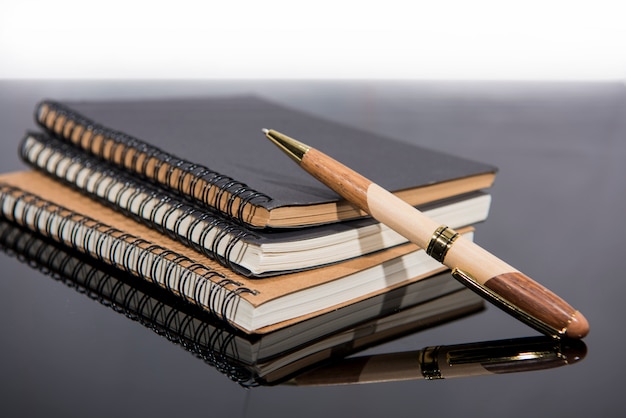 Dossiers, papier et stylo sur table en verre noir.