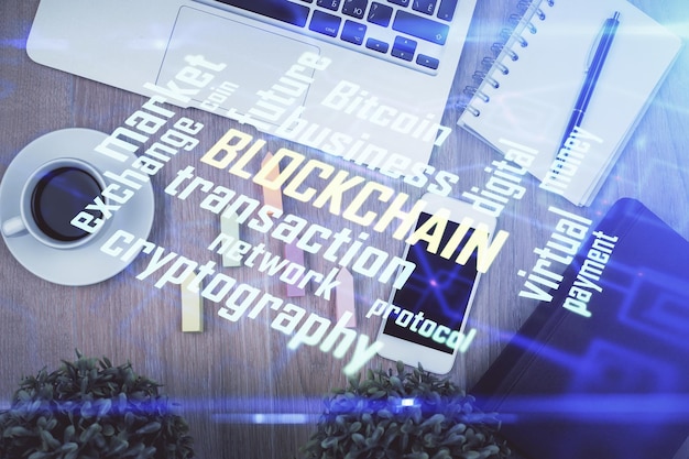 Double exposition de l'hologramme du thème blockchain sur la table avec le téléphone Vue supérieure Concept de technologie crypto