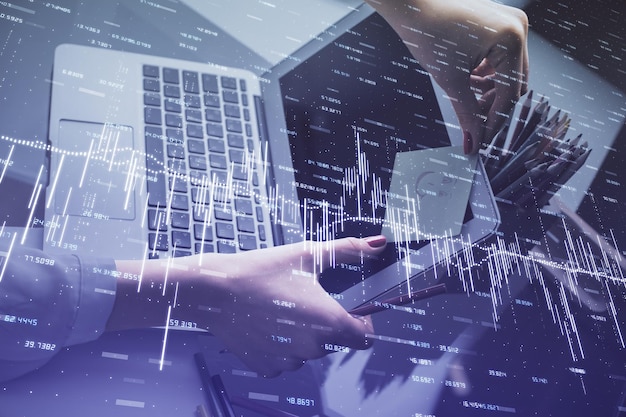 Double exposition des mains d'une femme d'affaires en train de taper sur un ordinateur et en train de dessiner un hologramme de graphique financier Concept d'analyse du marché boursier