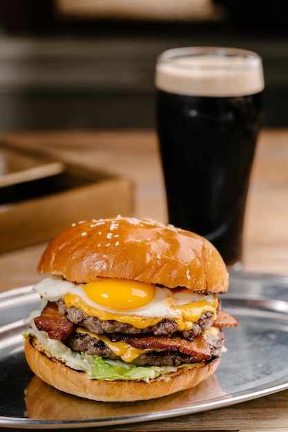 Double patty burger avec bacon de boeuf marbré fromage cheddar oeuf frit tomates oignons sauce à la crème et ketchup Table en bois au café