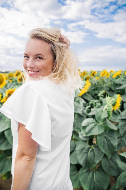 Douce belle fille en robe blanche dans un champ de tournesols s'amusant