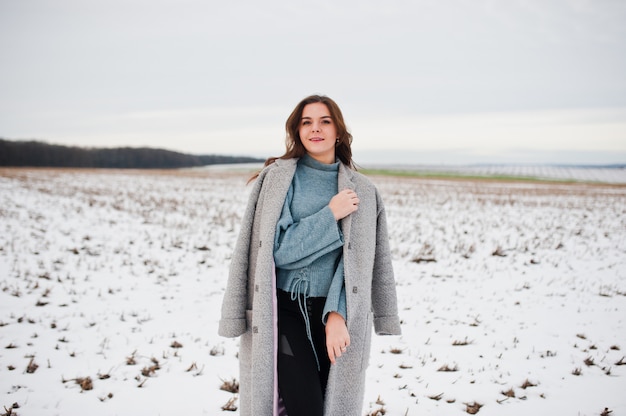 Douce femme en manteau gris contre le paysage enneigé.