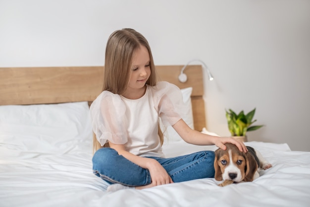 Douce fille assise sur le lit et jouant avec son chiot