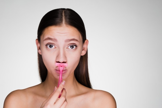 La douce fille triste se rase la moustache avec un rasoir rose