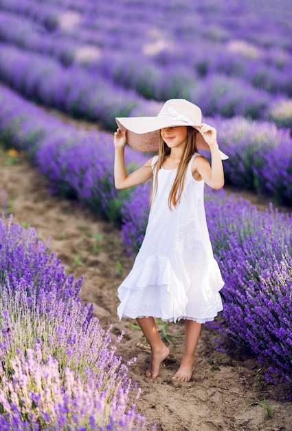 Douce jeune fille dans un champ de lavande. Un grand chapeau et une robe d'été blanche dessus.