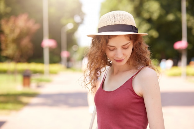 Douce jolie jeune femme debout au milieu du parc, regardant de côté, profitant du temps en plein air, portant des vêtements d'été décontractés