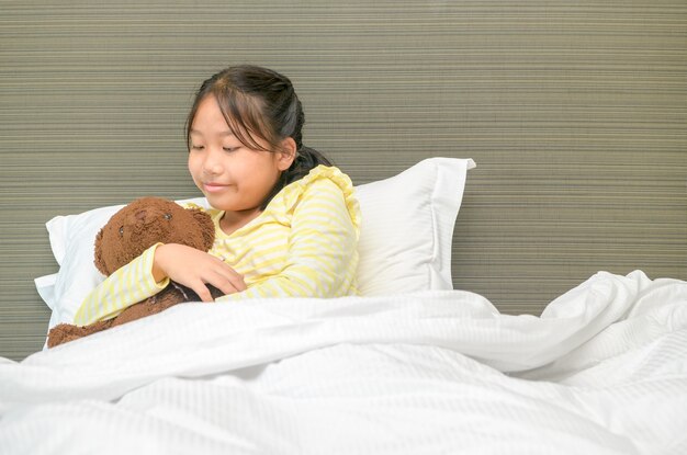 Douce petite fille étreint un ours en peluche, regardant l'ours et souriant en position couchée sur son lit à la maison