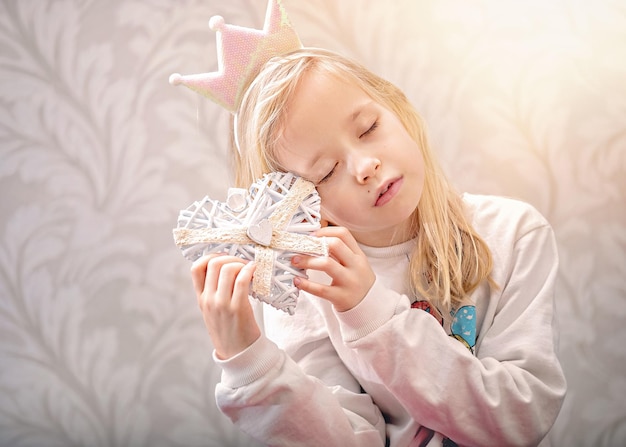 Douce petite fille tient un coeur de valentines et pense à l'amour, isolé sur fond gris