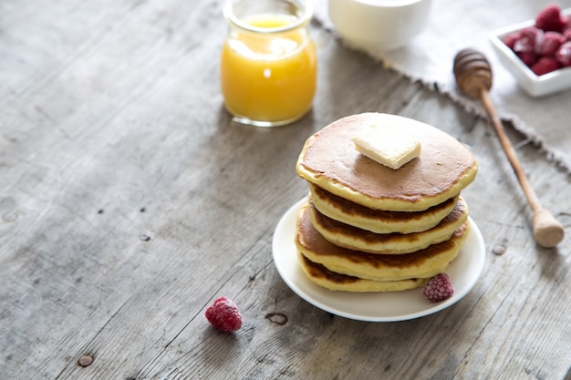 Douce pile de crêpes maison avec beurre, framboises et miel au petit-déjeuner