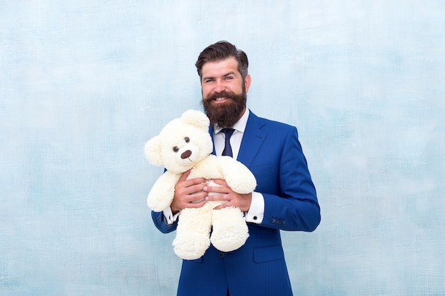 Doucement doux et idéal pour les câlins. Heureux homme d'affaires tenir fond bleu jouet ours en peluche. Homme barbu sourire avec peluche. Magasin ou magasin de jouets. Le jouet fait un excellent cadeau.