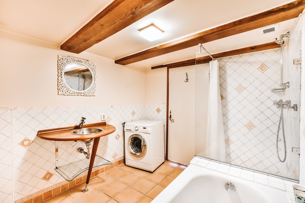 Douche et baignoire dans salle de bain lumineuse avec machine à laver et table en bois avec lavabo sous poutres en bois