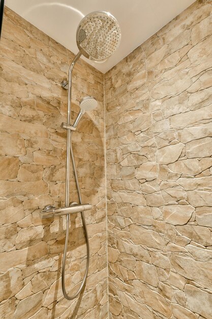 une douche qui est dans une salle de bain avec des murs en pierre et des carreaux sur le mur à côté il y a une douche à la main