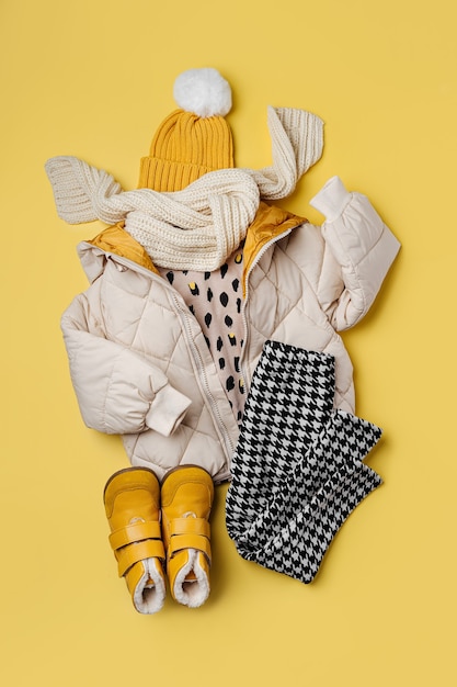 Photo doudoune chaude pour enfants avec chapeau et bottes sur fond jaune. vêtements d'extérieur élégants pour enfants. tenue de mode d'hiver