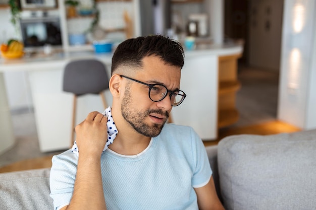 Douleur au cou jeune homme massant le cou endolori souffrant de douleur assis sur le canapé dans le salon à la maison Concept de problème de santé de l'arthrose