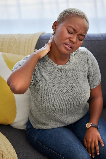 Photo douleur au cou de stress et femme noire fatiguée sur un canapé avec blessure dans le salon de l'appartement douleur musculaire et anxiété d'épuisement