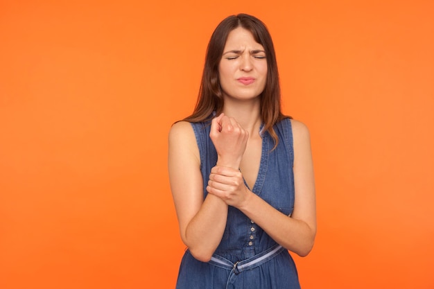 Douleur, bras douloureux. Femme malsaine tenant la main douloureuse et grimaçant de douleur, souffrant de traumatisme ou d'arthrite, syndrome du canal carpien. studio d'intérieur tourné isolé sur fond orange