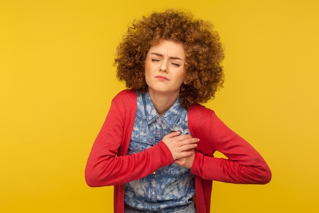 Douleur dans la poitrine Portrait d'une jeune femme déprimée fronçant les sourcils et touchant le sein risque de cancer se sentant mal au coeur aigu infarctus du myocarde tourné en studio intérieur isolé sur fond jaune