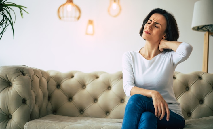Photo la douleur du cou. photo en gros plan d'une belle fille assise sur un canapé et souffrant de douleurs à la nuque.