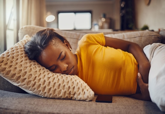 Douleur à l'estomac maladie et maladie obligeant une jeune femme noire fatiguée et endormie à faire la sieste et à se reposer sur un canapé à la maison Femme malade ou malade détendue souffrant de fatigue covid pendant la sieste